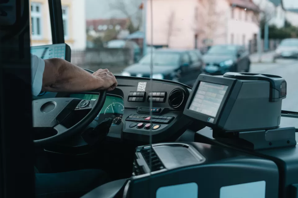 CLose-up of bus driver from behind with only hand on steering wheel visible.